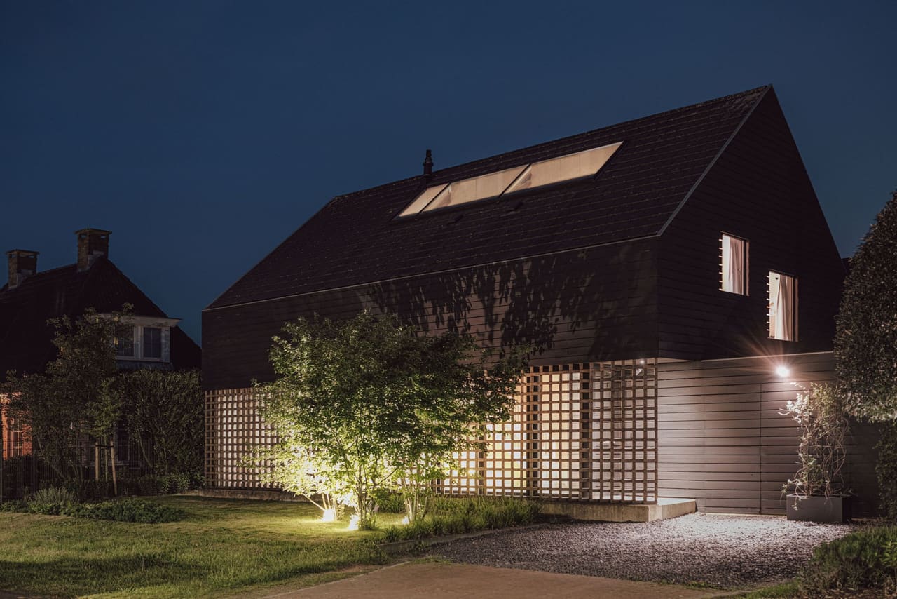 Filter House in Almelo bij avond: zwart houten huis met een opengewerkte gevel van baksteen waar het licht doorheen valt