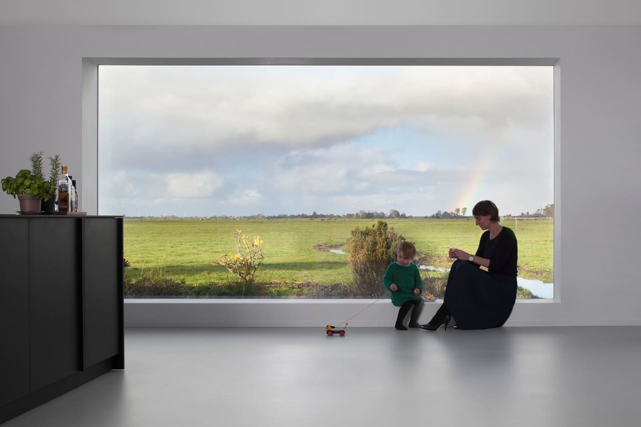 View House Edam: een groot raam in een witte woonkamer kadert de polder, met een moeder en kind op de vensterbank