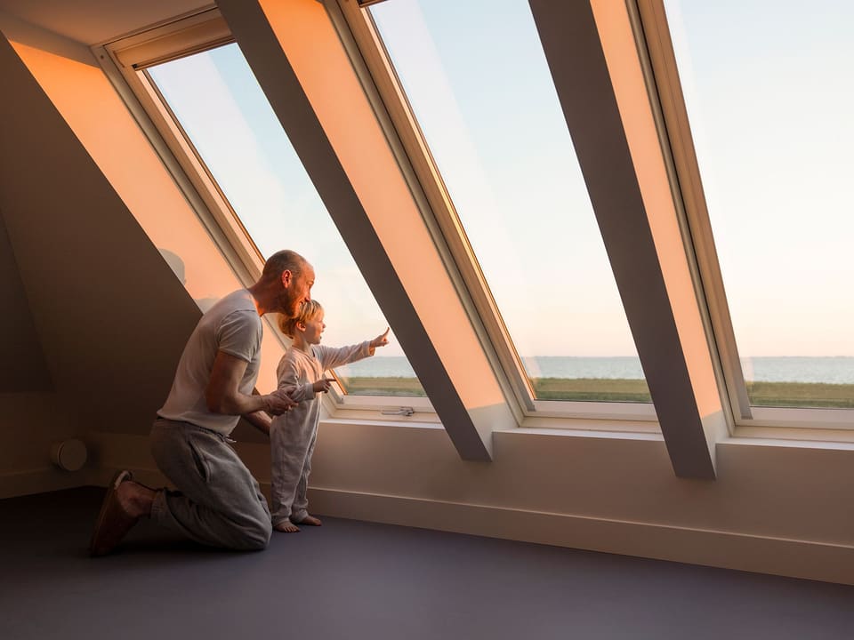 Een vader en kind kijken vanuit de slaapkamer in de punt van het dak door een dakraam naar het IJsselmeer
