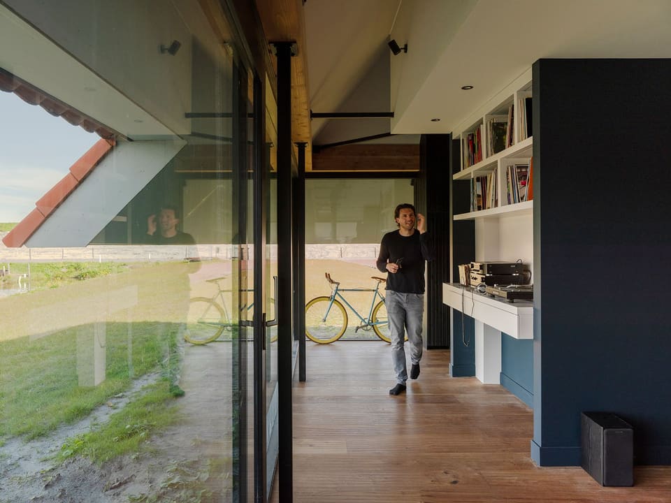 Bewoner in de leefruimte; achter het glas de polder en de dijk