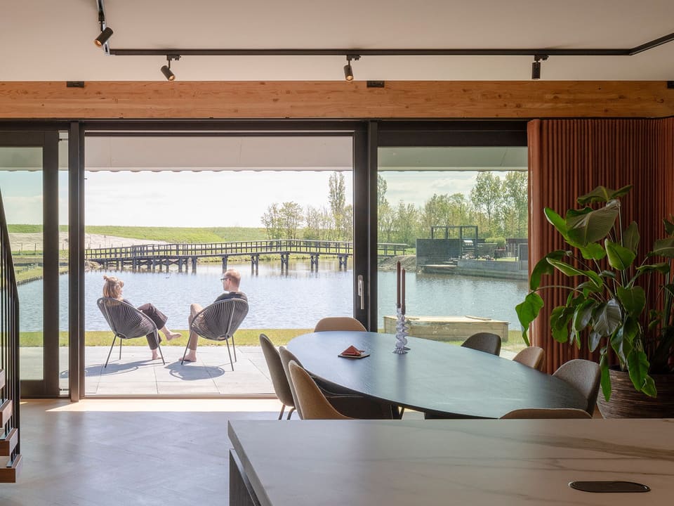 Eettafel aan het glas; buiten zitten twee mensen op het terras aan het water