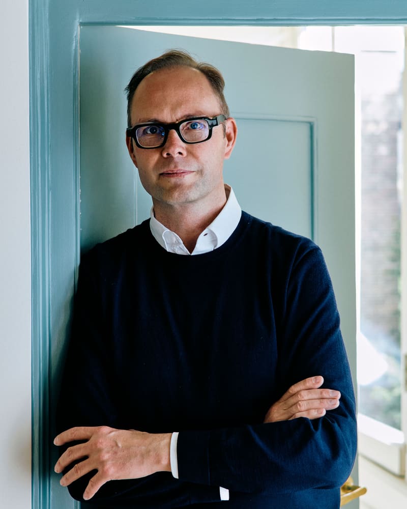 Portret van Geurt Holdijk in een donkerblauwe trui, leunend in een turquoise deurpost
